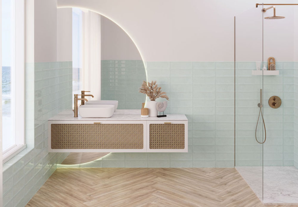 Baño elegante con combinación de materiales naturales y acabados metálicos. Mueble de baño de madera en blanco y ratán, encimera de mármol, grifería dorada y azulejos verdes menta. Suelo de parquet de madera en tono claro.