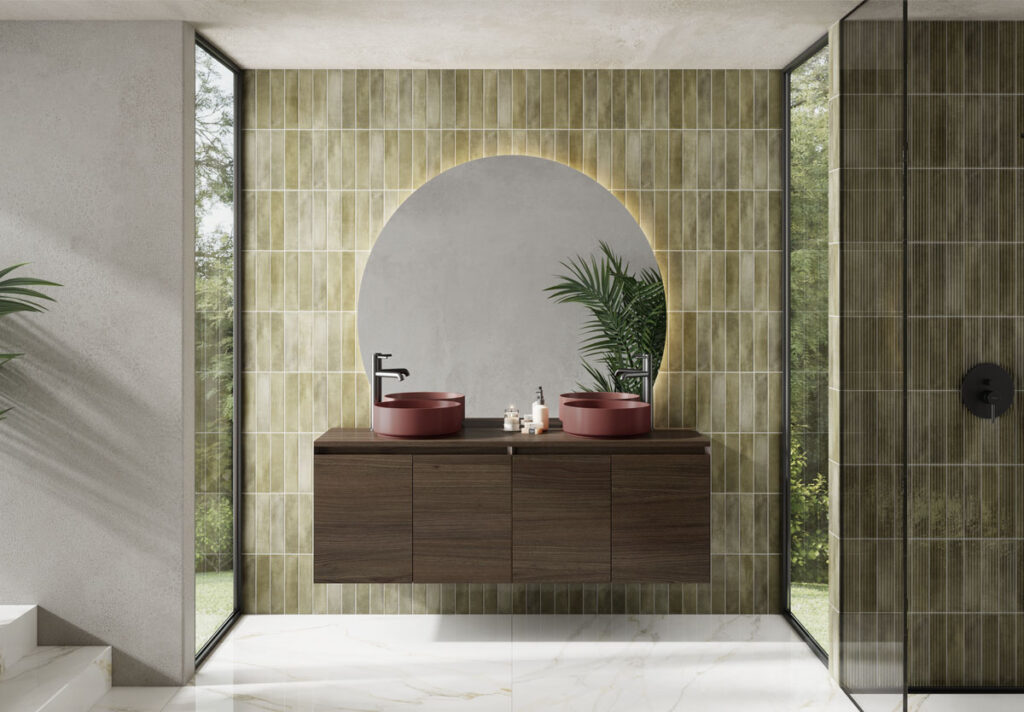 Mueble de baño suspendido de madera oscura con doble lavabo cerámico rojo y espejo redondo iluminado. Diseño moderno y sofisticado con revestimiento cerámico verde y suelo de mármol. Ideal para baños contemporáneos.